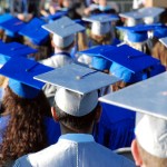 Graduates viewed from behind wearing graduation caps and gowns.