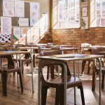 Empty classroom with wooden desks, table and chairs.
