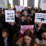 A group of protestors, many of them children, hold up anti-gun violence signs.