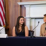 Three women look at each other while seated at a table.