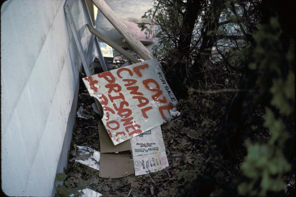 A hand-painted protest sign reading “Love Canal Prisoner” sits atop demolition debris in the neighborhood in 1982.