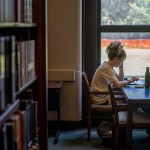 A students sits at a desk in a college library.